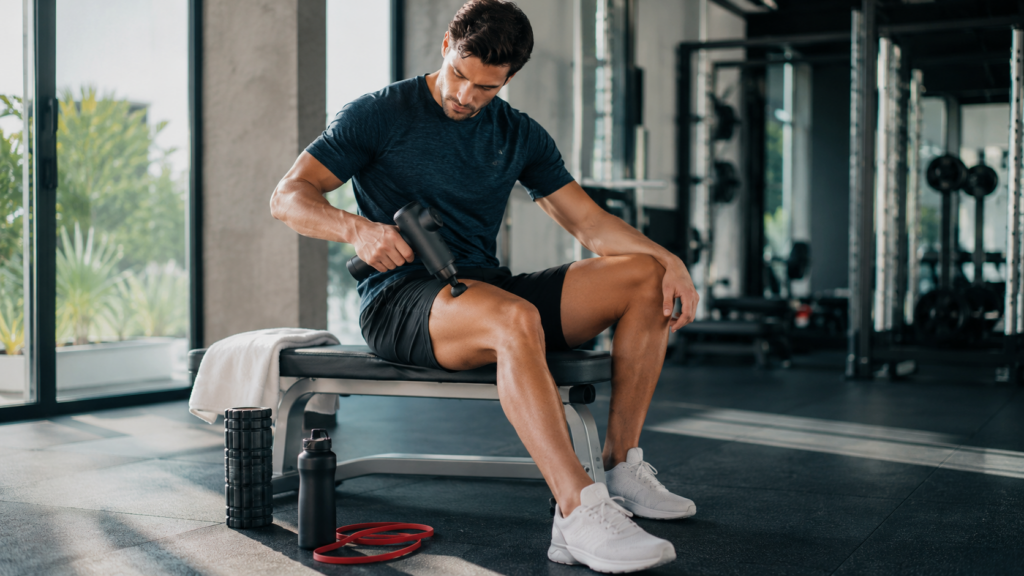 Athlete using massage gun carefully on sore thigh after workout to avoid recovery tech injuries